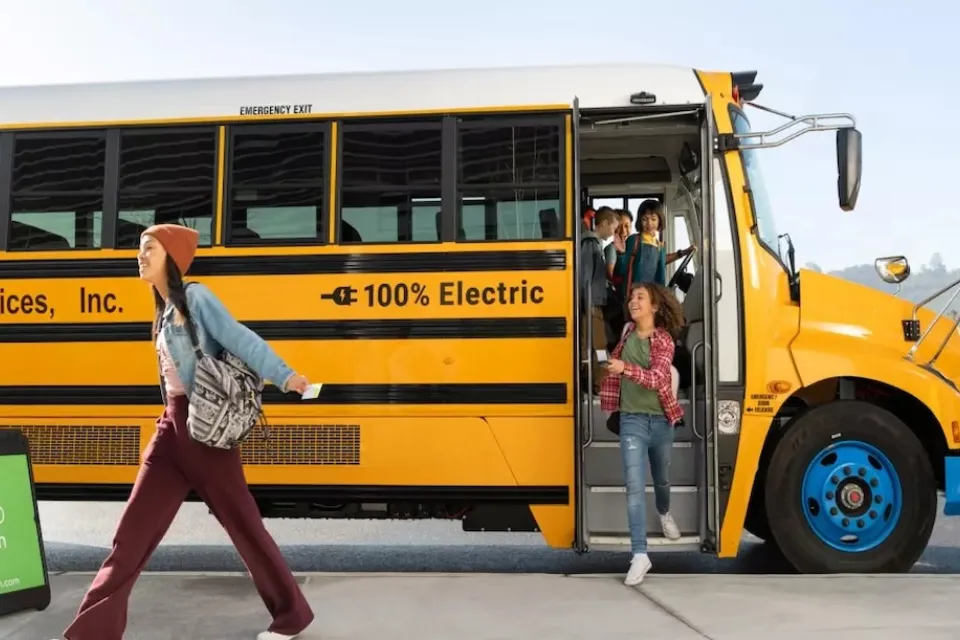 Yellow electric school bus with preteen students exiting.